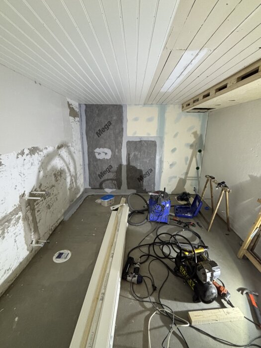 Ett rum under renovering med verktyg, byggmaterial och isolering på väggarna.