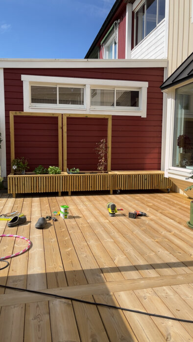 Nybyggd altan med trägolv och rödmålad vägg, inkluderar möbler och verktyg spridda över ytan, med himlen synlig i bakgrunden.