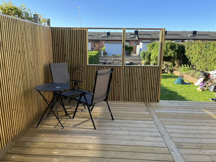 Altan med träväggar, två stolar och ett litet bord, samt utsikt mot en trädgård.