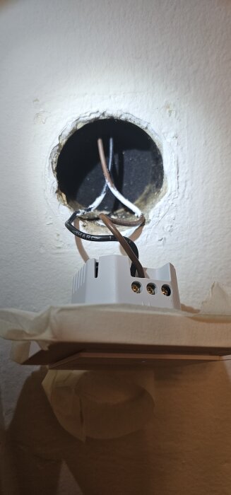 Elektrisk hål i vägg med två synliga kablar (brun och svart); ingen apparatdosa. En smart brytare kan anas under hålet.