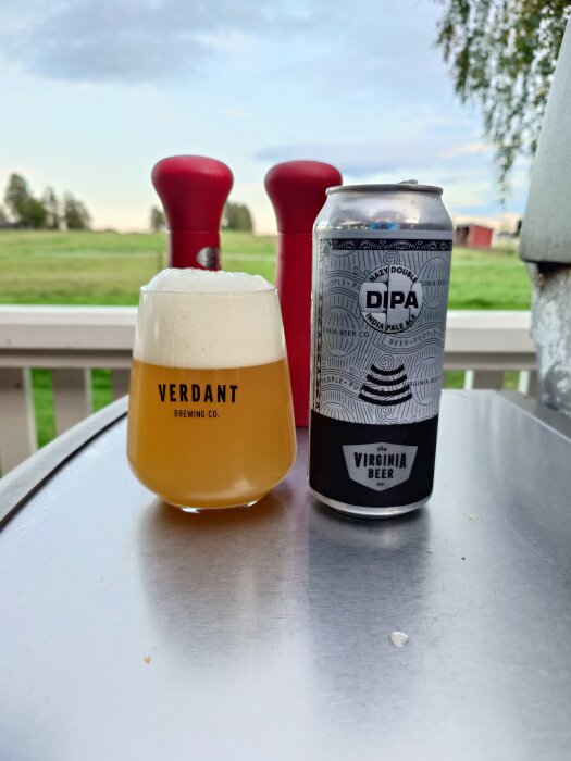 Fylligt öl i glas bredvid burk på bord, omgiven av natur.