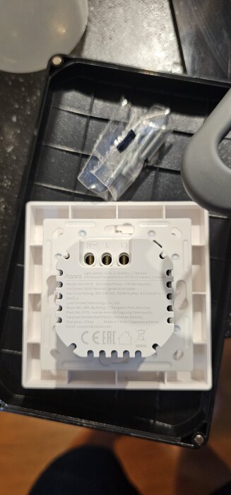 Vit Aqara ljusbrytare H2 EU med fyra anslutningar märkt N, L, L1 och opt, placerad på ett svart underlag med skruvar bredvid.