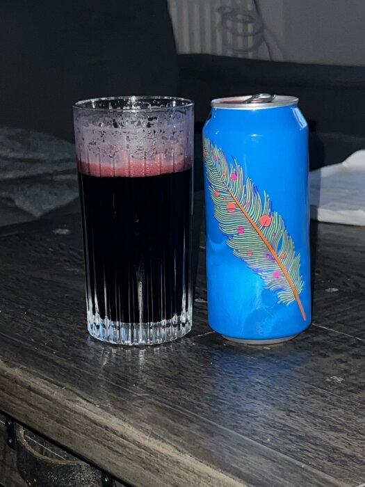 Dryck i glas med skumkant och burk med färgglad fjäder på träbord.