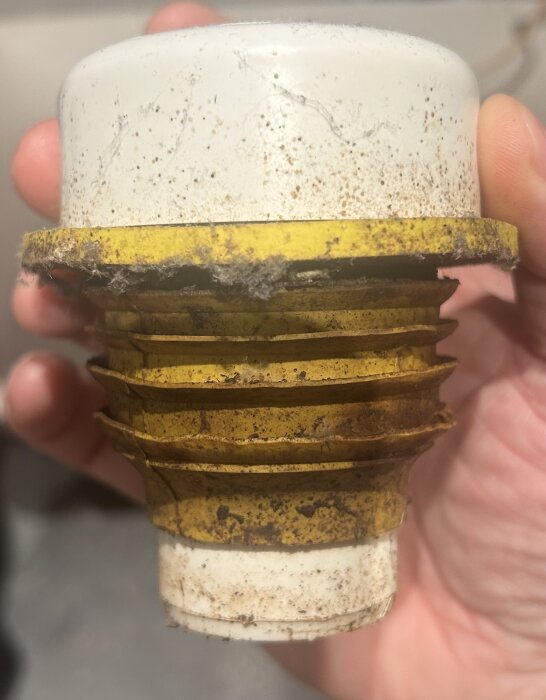 Gammal och smutsig gjutjärnsavluftare, Purus 40, med gula och vita delar hålls i handen. Letar efter adapter för denna avloppstätning.