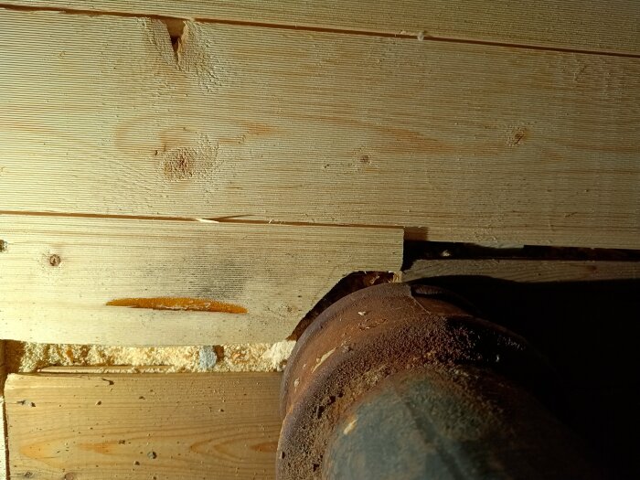 Närbild på ett trägolv med en del av ett rör synligt. Golvet verkar nyligen ha blivit reparerat eller utbytt.