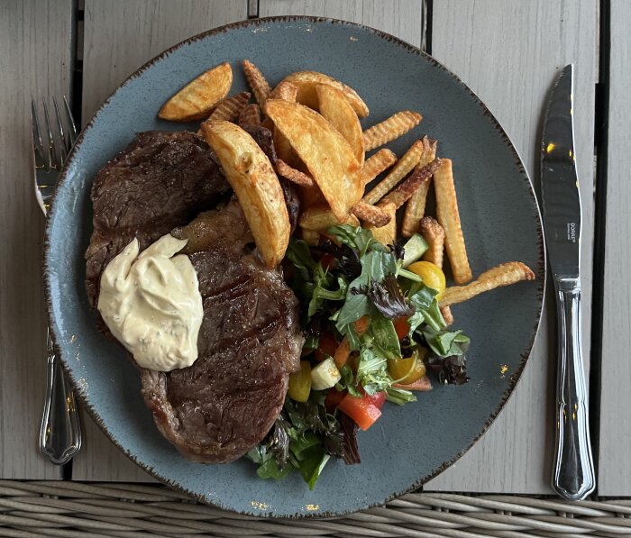 Grillad entrecote, serverad med pommes och sallad på tallrik.