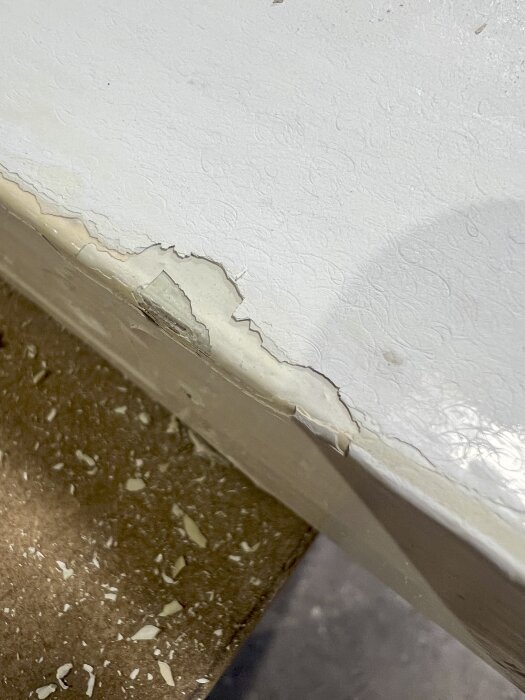 Flagnande vit färg på gammal dörr, synlig spricka vid kanten och färgflagor på golvet.