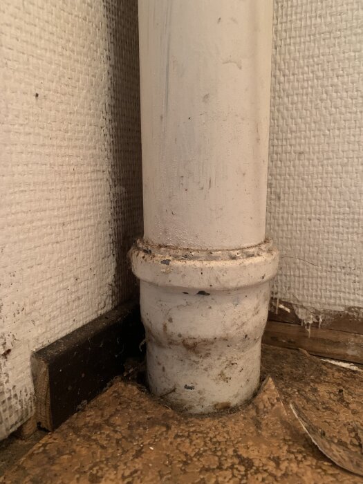 Rörgenomföring genom golvspånskiva med synlig fukt och mögel runt röret.