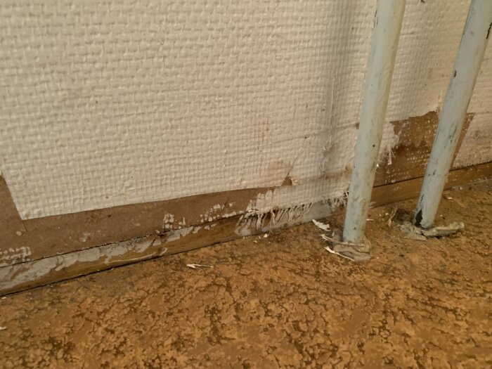 Rörgenomföringar genom golvspånskiva med tecken på fukt och mögel.