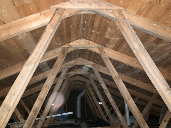 Takstolar av trä i ett vindsutrymme med synliga fackverk och trätak.