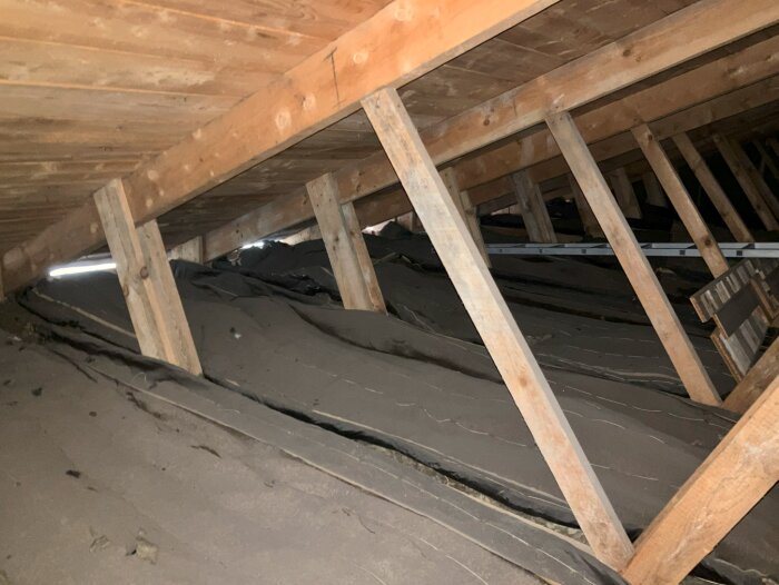 Bilden visar takstolar av fackverk och bjälkar på en vind med synliga reglar, som delvis är täckta av isoleringsmaterial.