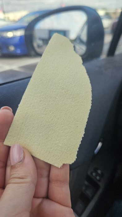 Gul provbit av Tassos väv hålls i handen, med slät yta och något ojämn kant, tagen i en bil med backspegel i bakgrunden.