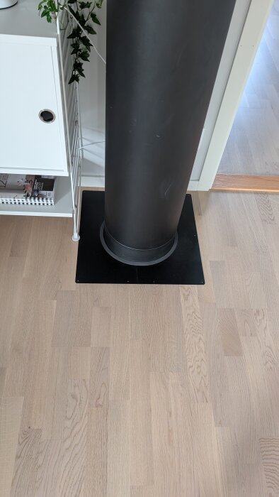 Svart rökrörshölje ovanpå parkettgolv bredvid vit bokhylla.