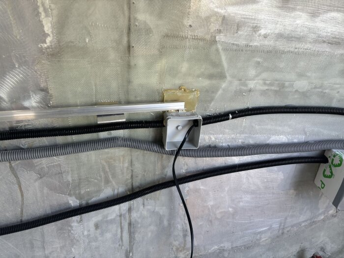 Elektriska rör och dosor fastsatta på en vägg täckt med tunn skumisoleringsskikt, med en förskjuten dosa och exponerade elslangar.