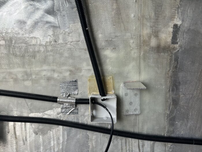 En vägg med eldosor, plastslangar, silvertejp och ett fäste. Förberedelser inför sprayfoam-isolering.