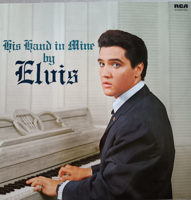 Omslag till Elvis Presleys album "His Hand in Mine", där han sitter vid ett vitt piano i kostym.