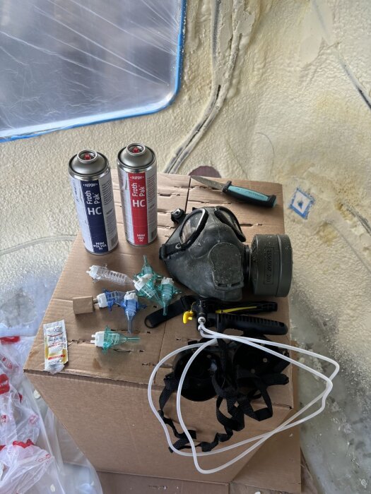Kartong med två Froth Pak HC-sprayer, gasmask, sprutmunstycken och kniv för förberedelse av sprayfoam-isolering.