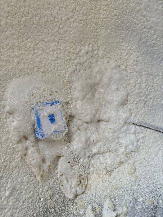 Närbild av sprayfoam på vägg med ojämn yta och synlig eluttag, omgiven av luftbubblor och ojämnt fördelat skum.