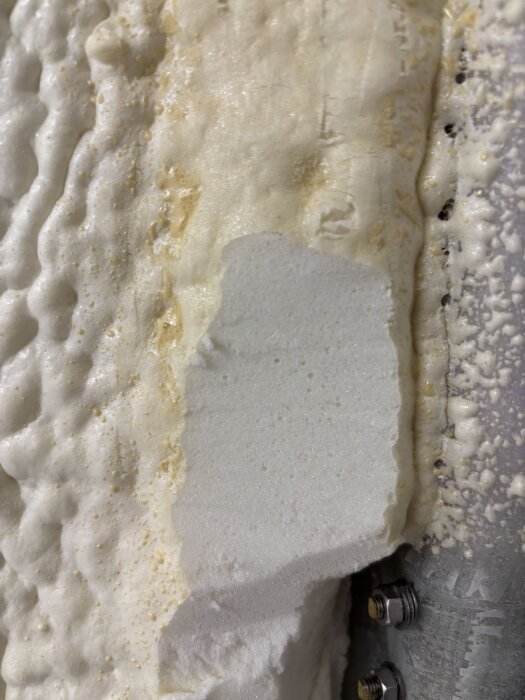 Trimmat sprayfoamskum på en yta med synliga lager, blandning av tätt och öppet skum, visar skillnader i struktur och kvalitet.