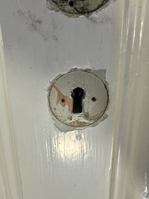 Runt nyckelhål utan beslag avlägsnat, visar två lager färg: grågrön och vit.