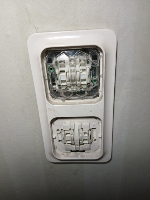 Två elektriska strömbrytardosor installerade på en vägg, med den övre dosan säkrad under ett skyddande plastskydd.