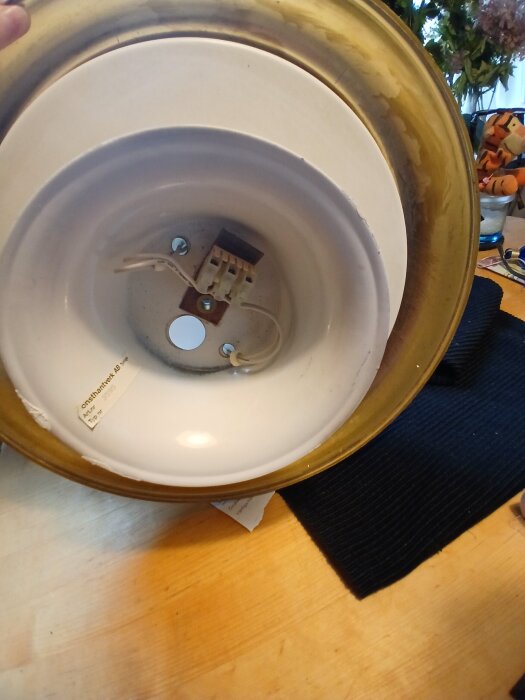 Elektrisk armatur sedd underifrån med delvis synlig ledning och kontakt, placerad på en träyta med mörk bakgrund.