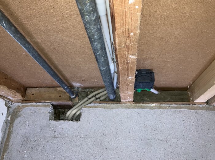 Rördragning och elinstallation i vägg bredvid betonggolv i källare med gips och träreglar synliga.