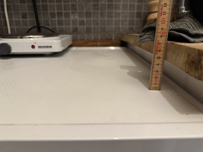 Mätning av avståndet mellan kylskåpets topp och en överliggande träskiva med linjal i köksmiljö.