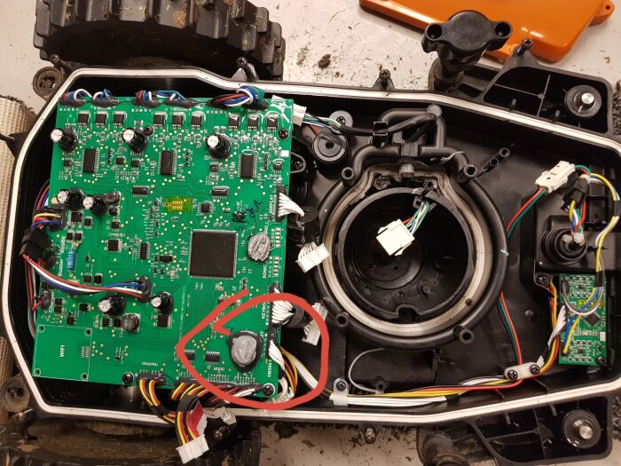 Elektronikkrets med knappcellsbatteri delvis täckt av lim och omringat av kablar, markerat med röd cirkel.