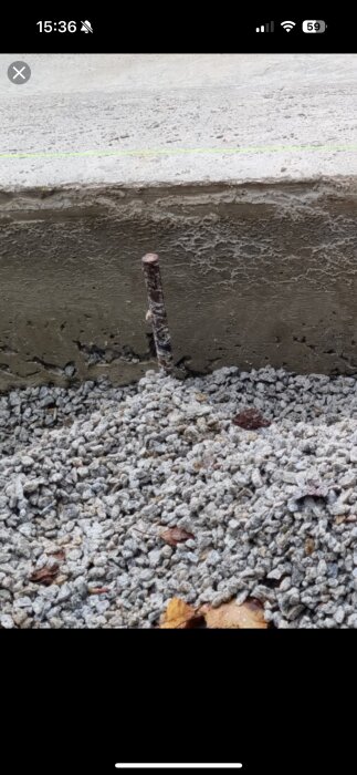 Betonggrund med synlig armeringsjärn som sticker upp, omgiven av grus.