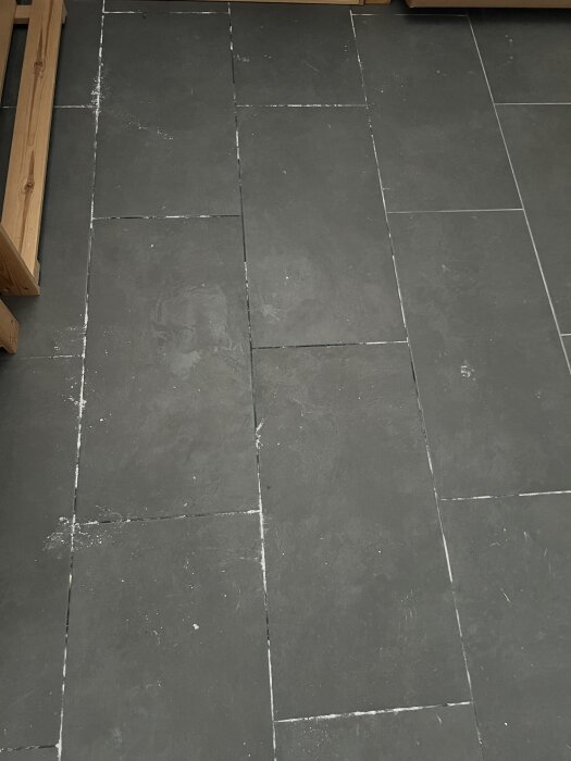 Svarta klinkerplattor med vita saltutfällningar i fogarna på ett källargolv.