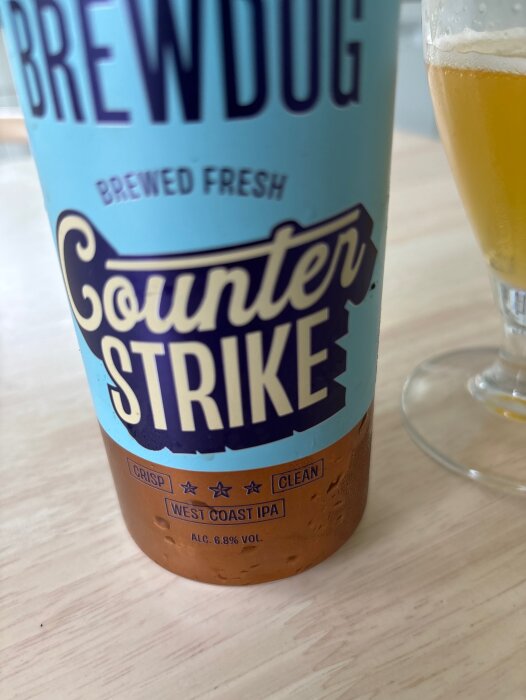 Flaska med etiketten "Brewdog, Counter Strike, West Coast IPA, 6.8% vol." bredvid ett halvfullt ölglas på ett bord.