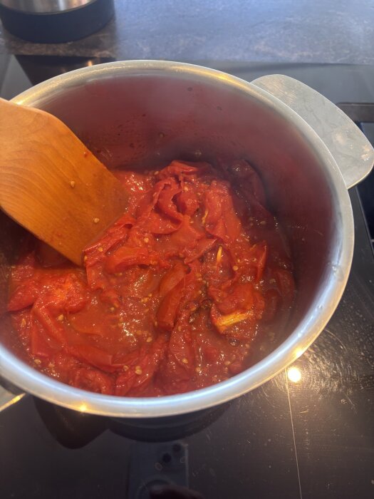 Tomatsås kokas i en kastrull med en träsked på spisen.