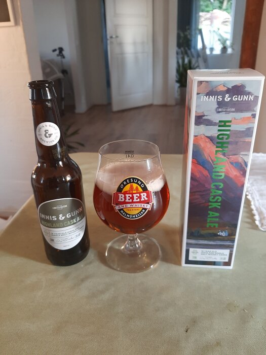 Flaska och glas med Innis & Gunn Highland Cask Ale bredvid förpackning på bord.