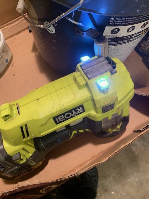 Gul Ryobi spikpistol med lysande lampor ligger på en pappkartong bredvid en dunk.