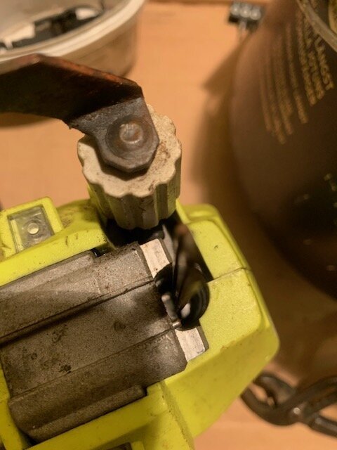 En närbild på en gul Ryobi spikpistol med metalliska delar och en justeringsskruv, delvis synlig i ett verkstadsområde.