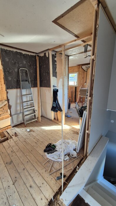 Renoveringsprojekt med nedriven vägg, stege mot tapetserad vägg och verktyg på trägolv.