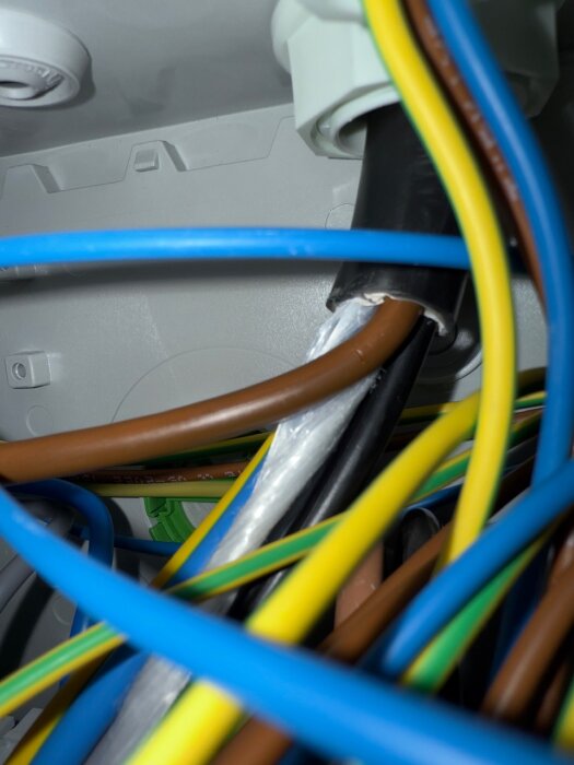 Brun kabel med skadat hölje i en elektrisk installation för elbilsladdare, synliga flerfärgade kablar i närheten.