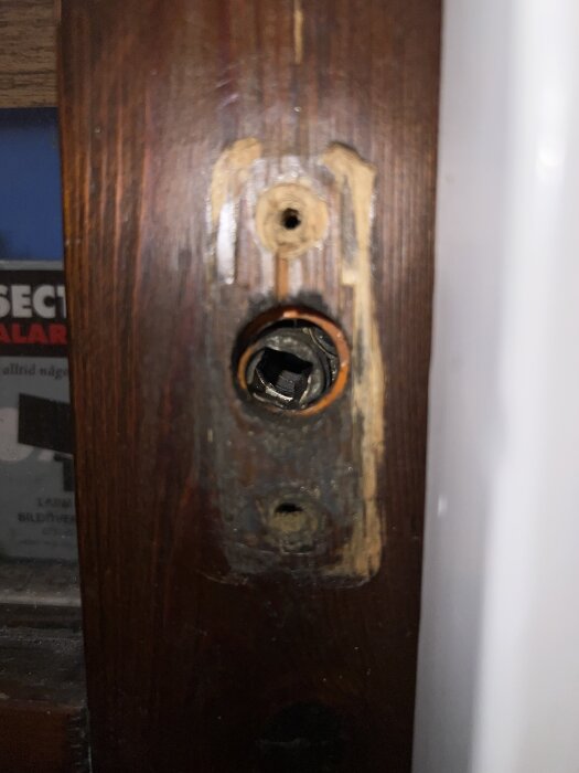 Roddarhål i en gammal träaltandörr, något skevt och slitet, där ett handtag ska monteras. Skruvhål och slitage synliga runt hålet.