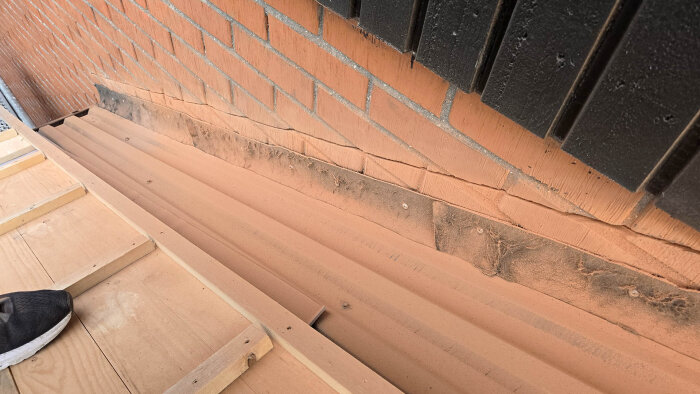 Tegeltak med nyinstallerad plåt vid vägganslutning, visar detalj av plåtens överlapp och anpassning nära tegel och trappa.