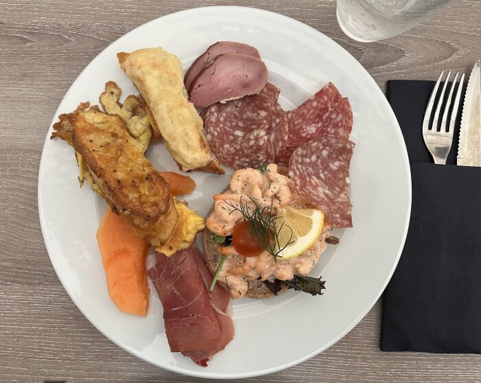 Blandad tallrik med fläskstek, lax, potatisgratäng, salamiskivor och andra delikatesser.