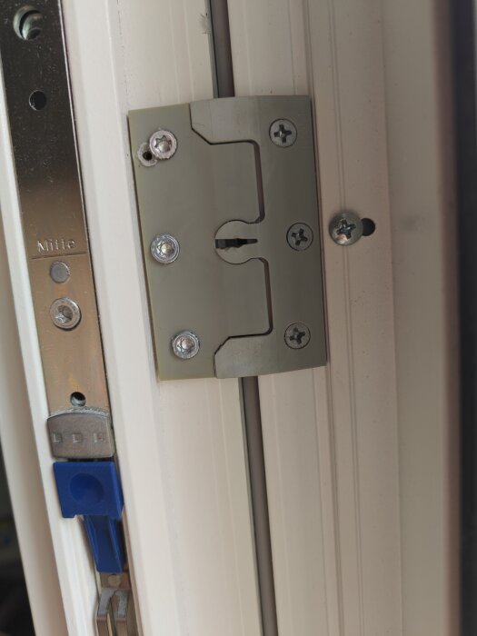 Fönstermekanism med flera skruvar och ett blått spänningslås, potentiellt modifierad med utbytta skruvar på en sida.