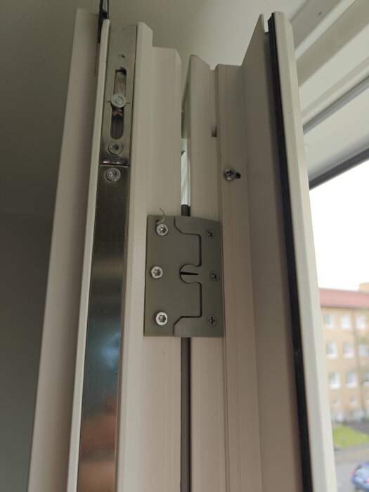 Fönsterhängsel och skruvmekanism syns i närbild på en vitmålad fönsterkarm med flera metallskruvar och beslag.