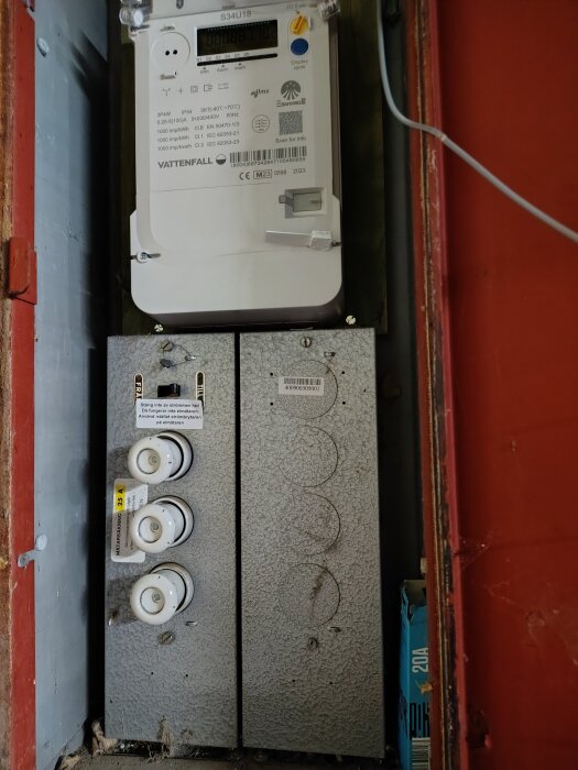 Elmätare och säkringspanel i ett icke-isolerat förråd. Bilden visar en elmätare ovanför en säkringsdosa.