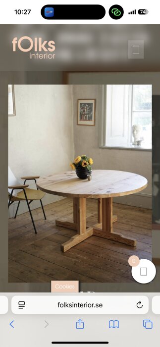 Runt matbord i furu med en vas med solrosor, placerat på ett trägolv i ett rum med stora fönster.