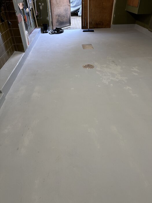 Matt och flammigt garagegolv målat med Hagmans EP-V epoxifärg, med viss blank yta; sladd och stövlar i bakgrunden.