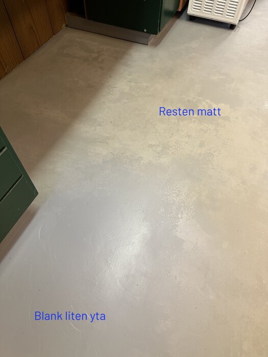 Bild på garagegolv med epoxifärg; en del är blank medan majoriteten av ytan är matt och flammig. Texter markerar "Blank liten yta" och "Resten matt".
