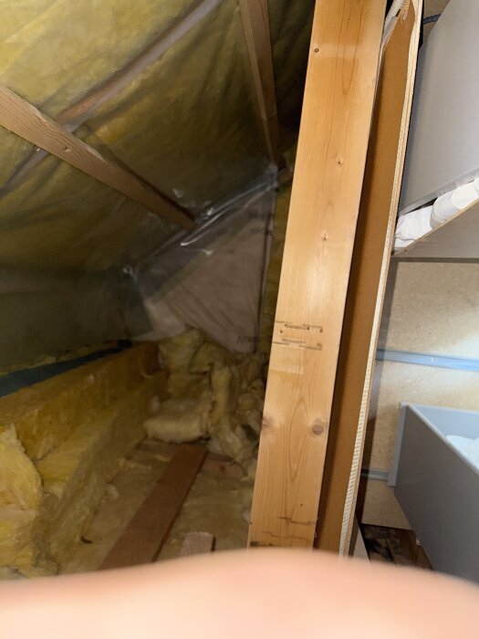 Isolering och träbjälkar i en kattvind med synlig gipsskiva och fragment av gul isolering.