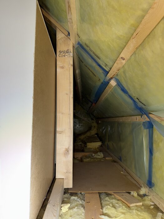 Öppen kattvind med gul glasfiberisolering i tak och väggar samt synlig träkonstruktion.