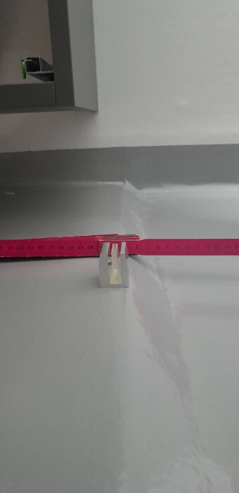 Måttband mäter avståndet mot en skåra i golvet där duschvägg ska monteras.